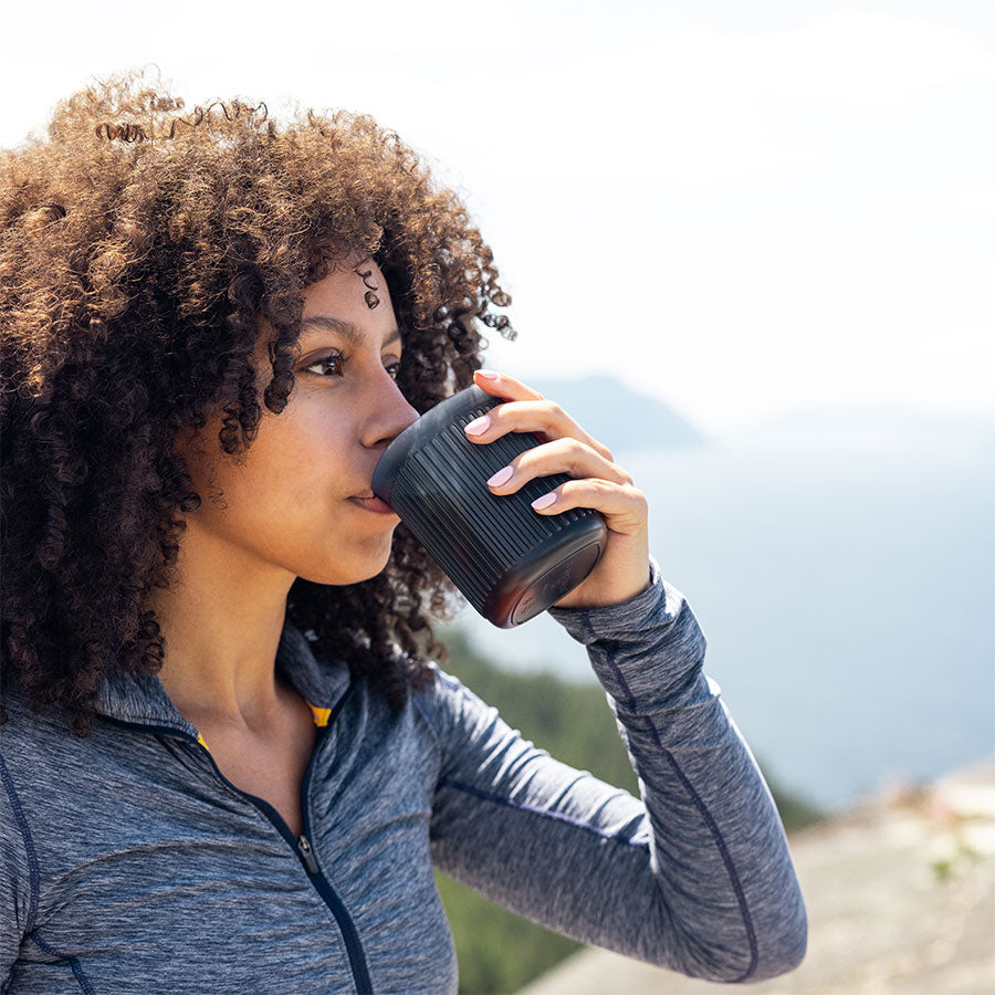 Frau trinkt Kaffee draußen mit Aerobie AeroPress Go Kaffee-Zubereiter inkl. 100 Filtern beim Wandern
