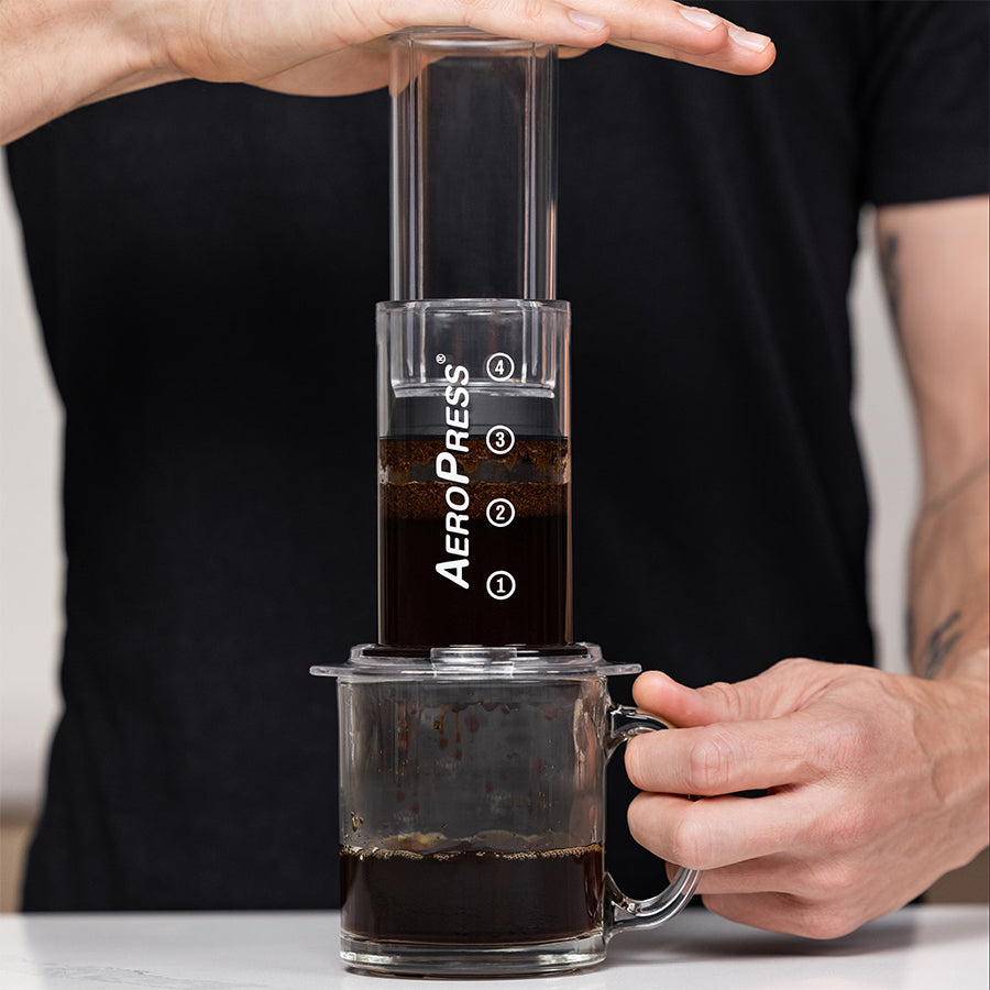 Aerobie AeroPress Kaffee-Zubereiter inkl. 100 Filtern mit frischem Kaffee in transparenter Tasse