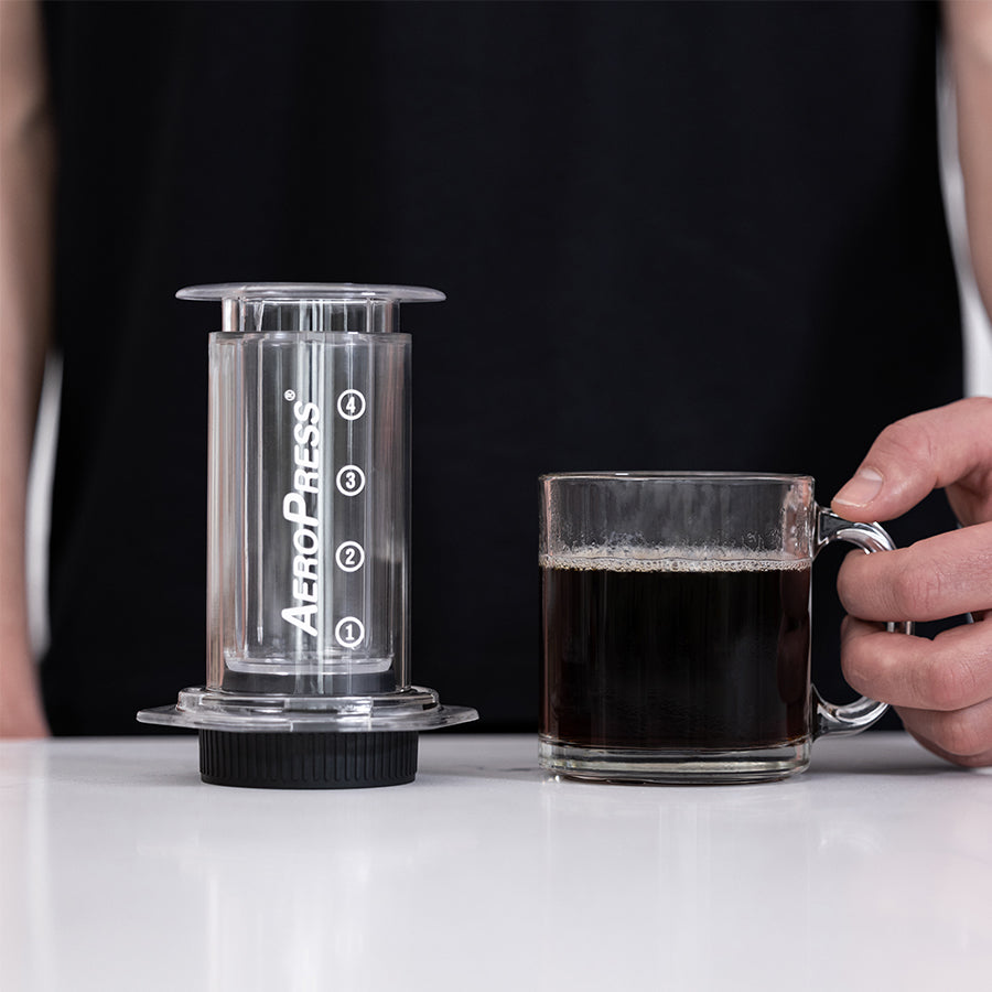 Aerobie AeroPress Kaffee-Zubereiter inkl. 100 Filtern mit frischem Kaffee in einer Glastasse