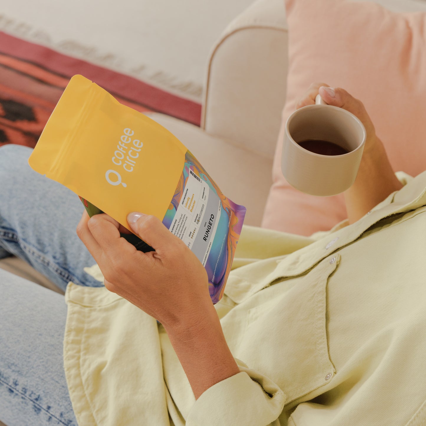 Person hält Rungeto Kaffee Verpackung und eine Tasse Kaffee entspannt auf dem Sofa sitzend