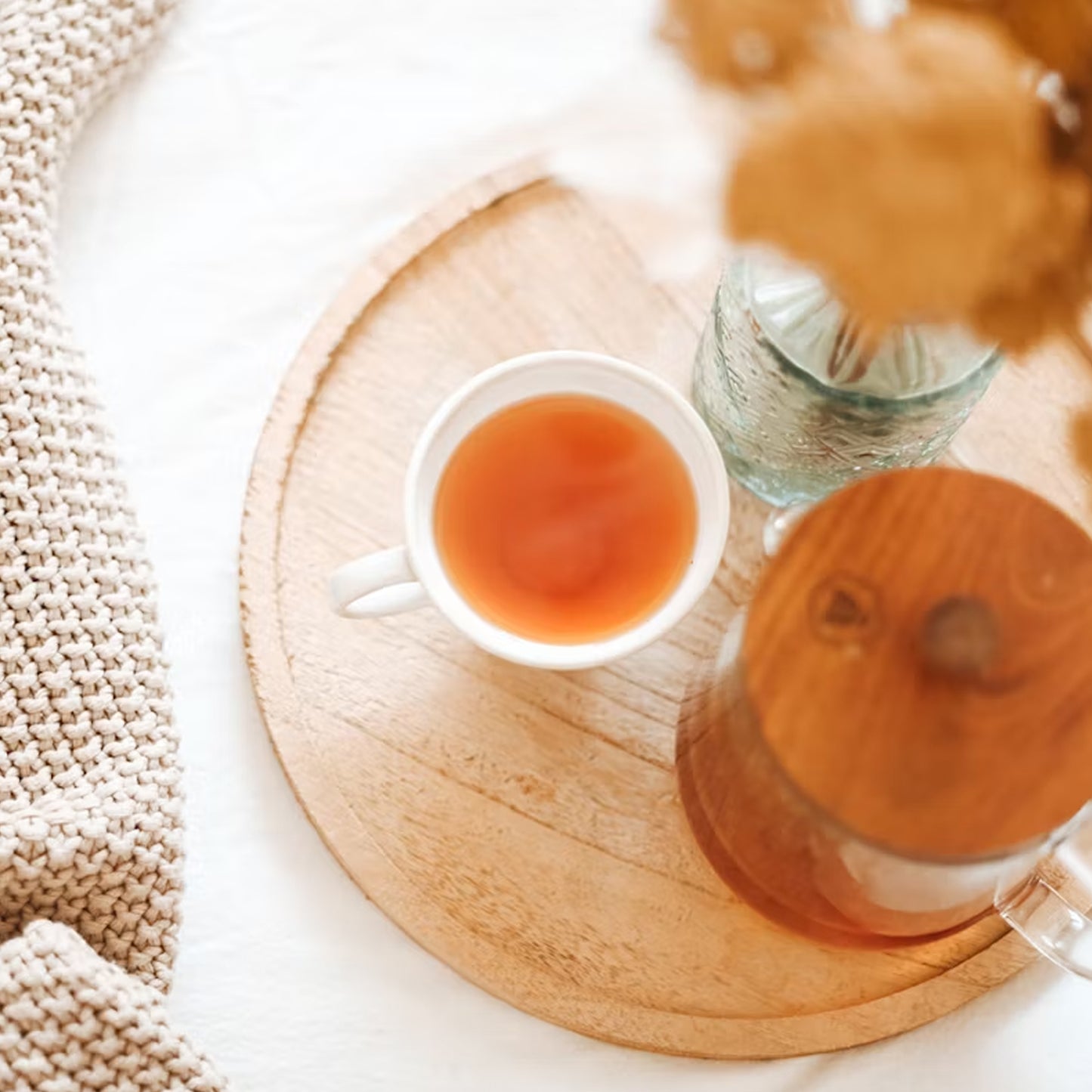 Cascara Tee in weißer Tasse und Kanne auf Holztablett mit gemütlicher Strickdecke daneben