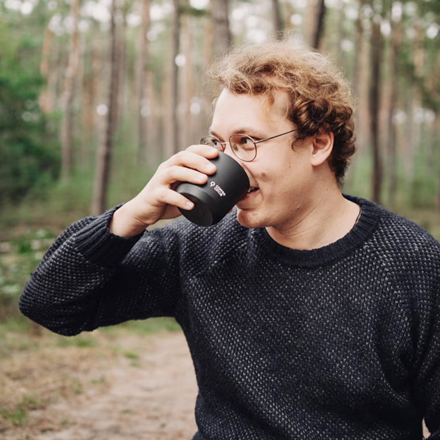 Mann genießt Kaffee aus einem Becher mit Drip Bags im Wald – einfacher Kaffee unterwegs mit Drip Bags.
