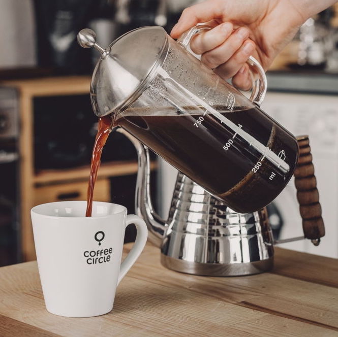 French Press & Kaffee im Set: Kaffee aus Trendglas Jena French Press in Tasse eingegossen.